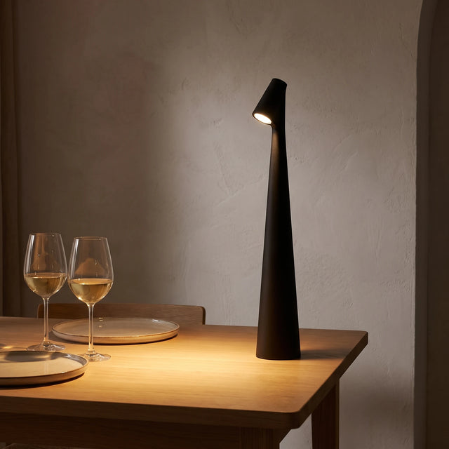 Lámpara Faro encendida sobre una mesa de comedor de madera clara, luz cálida en un ambiente japandi