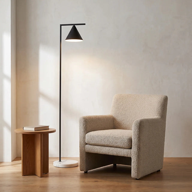 La lámpara en un rincón de lectura, junto a un sillón de bouclé y una mesa lateral de madera