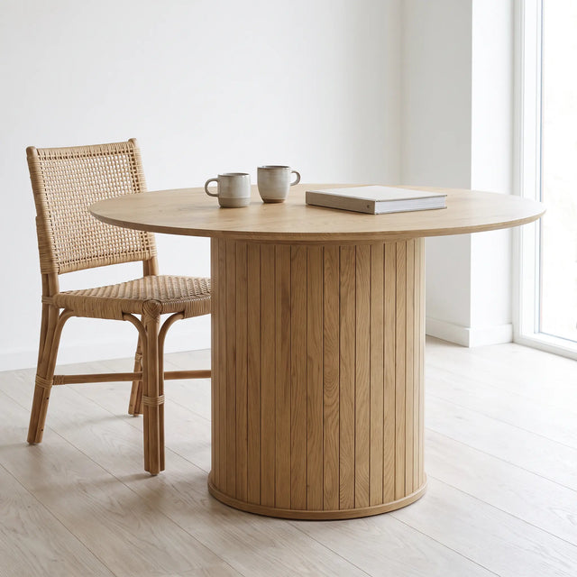 Mesa Koma de 120 cm junto a una silla de ratán, dos tazas y un libro para ver su escala