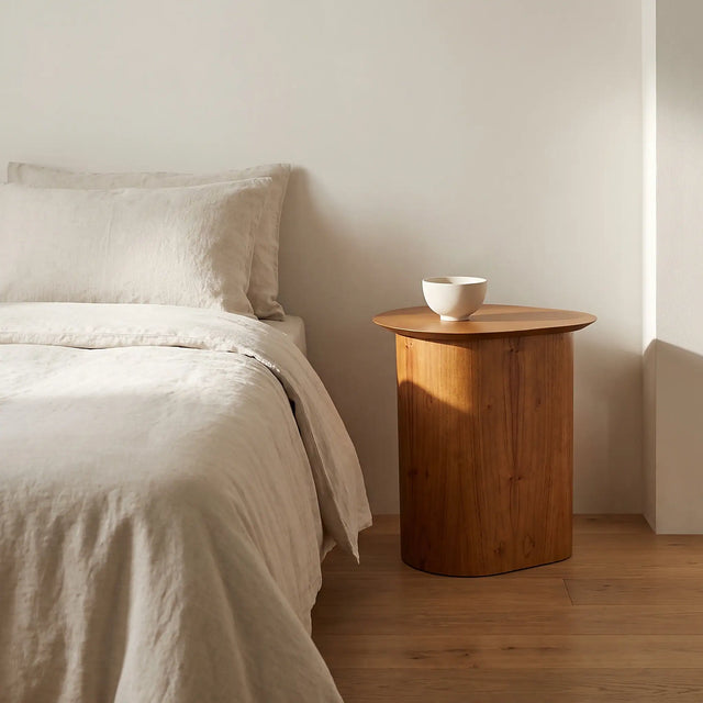 La mesa usada como velador junto a una cama vestida en lino color hueso