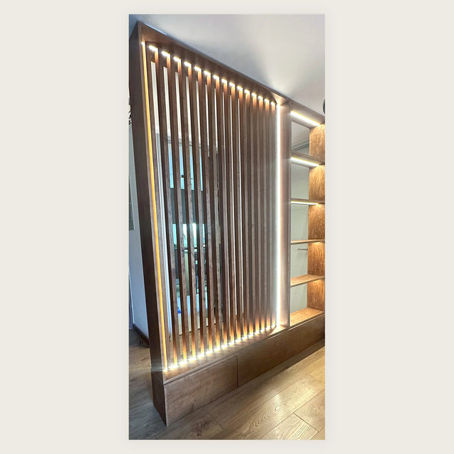 Mueble divisorio a medida con celosía de madera de piso a cielo, iluminación LED cálida y estantería