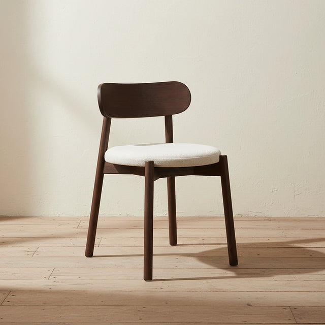 Silla de comedor Kaya sola contra un muro de yeso encalado en un interior wabi sabi