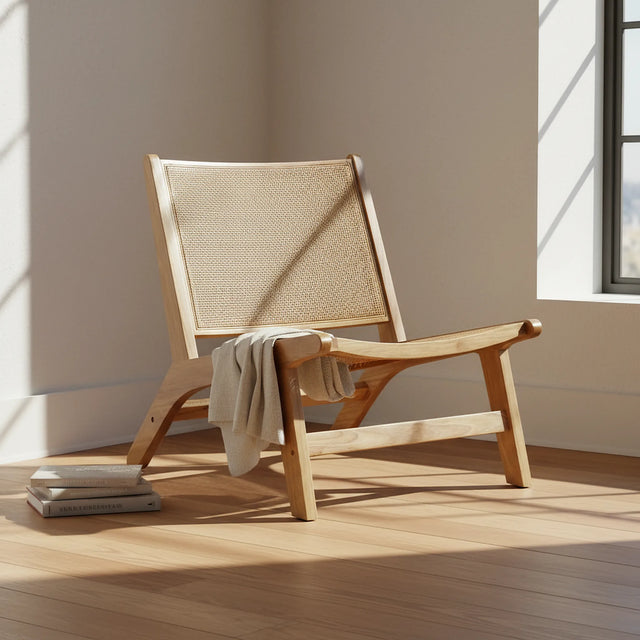 Silla lounge junto a una ventana con una manta de lino y libros sobre el piso de madera