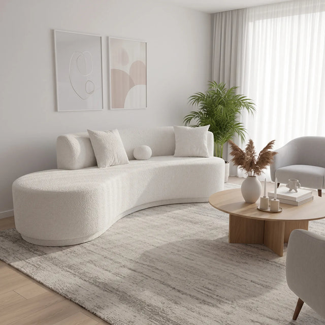 Sofá curvo Amaia en living japandi con mesa de centro de madera, planta y cuadros neutros