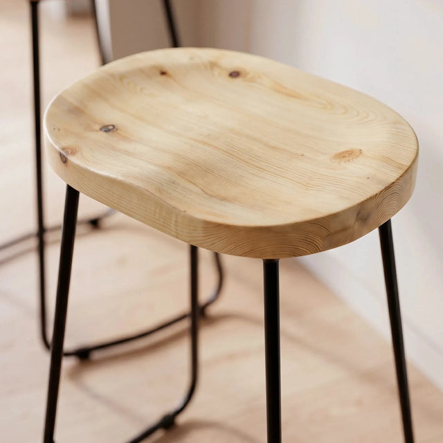 Primer plano del asiento contorneado de pino del Taburete Sumi en una cocina luminosa